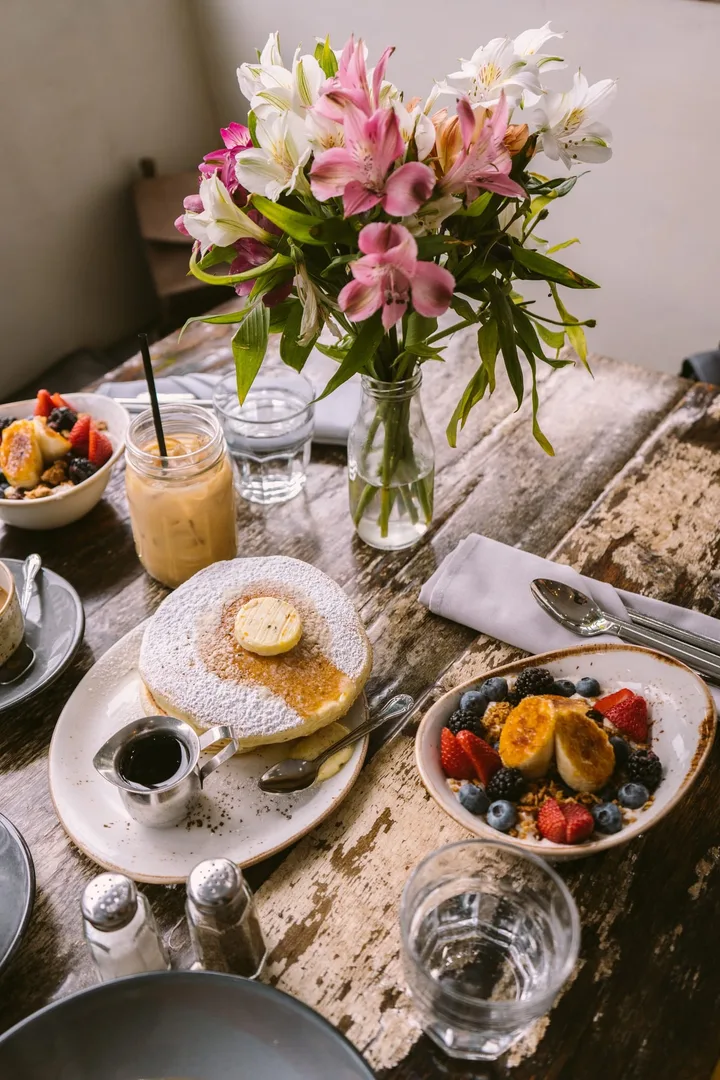 Table de petit-déjeuner avec bouquet de fleurs, pancakes, bols de fruits rouges, boissons et couverts