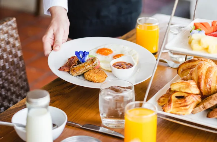 Petit-déjeuner avec œufs, viennoiseries, fruits, pain, jus d’orange et boissons chaudes sur une table dressée